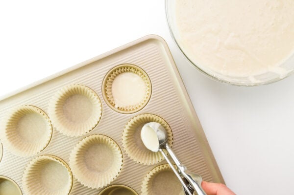 Cake batter is being distributed into muffin pan with a dispenser.