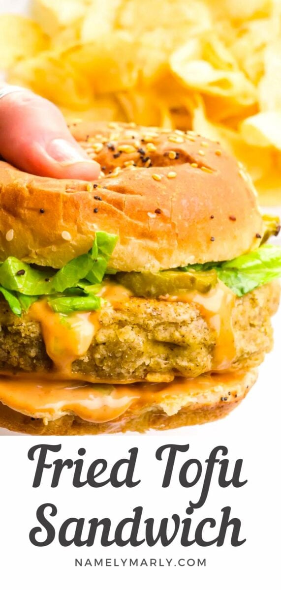 A hand holds a sandwich in front of a plate with potato chips. The text reads, Fried Tofu Sandwich.