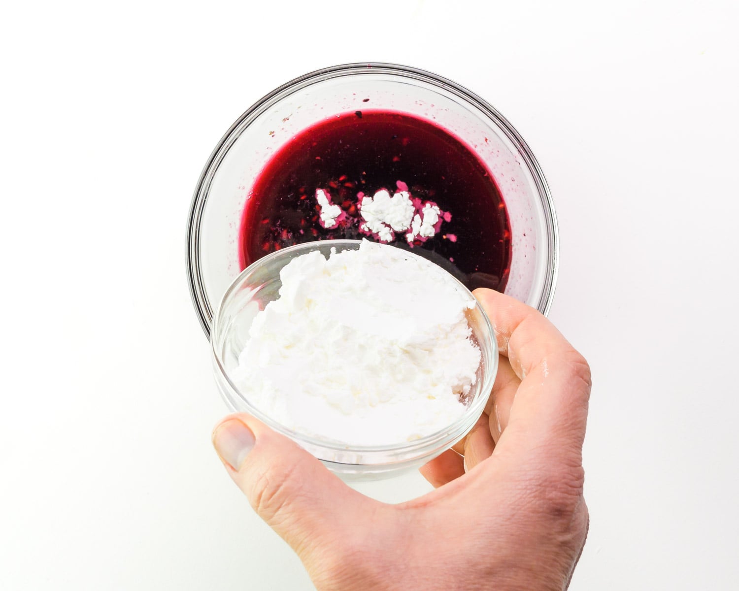 Cornstarch is being poured into a bowl with berry juice.