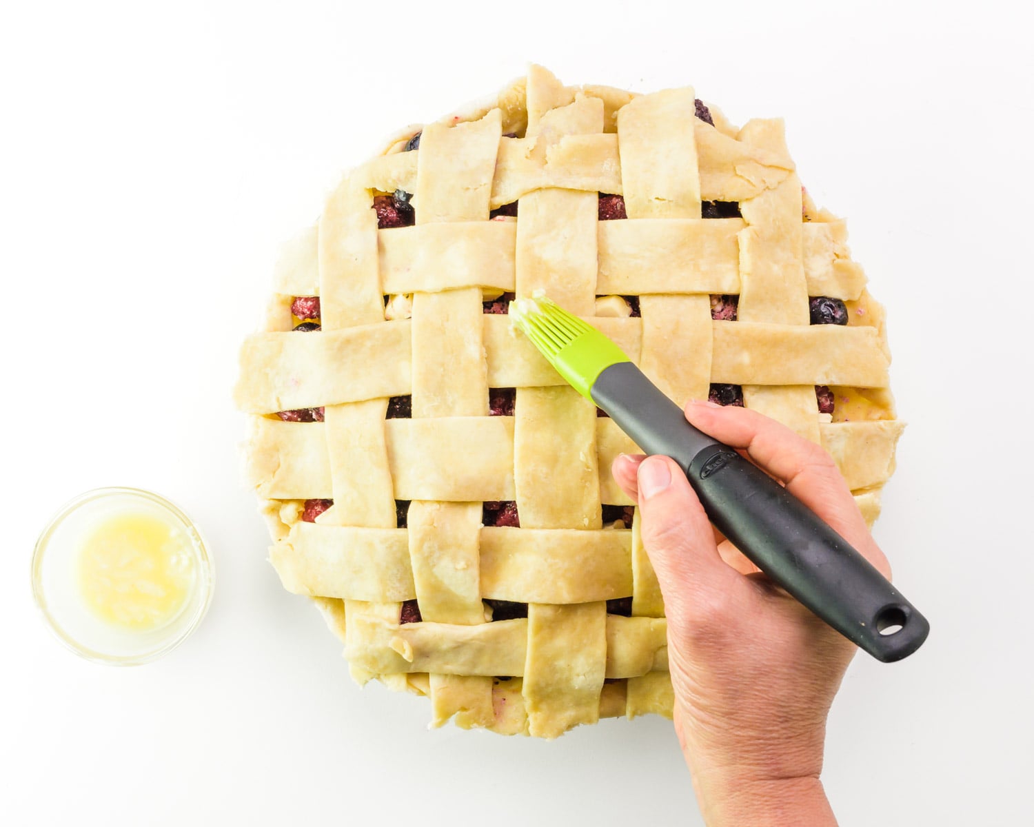 Vegan egg wash is being brushed over an unbaked pie crust.