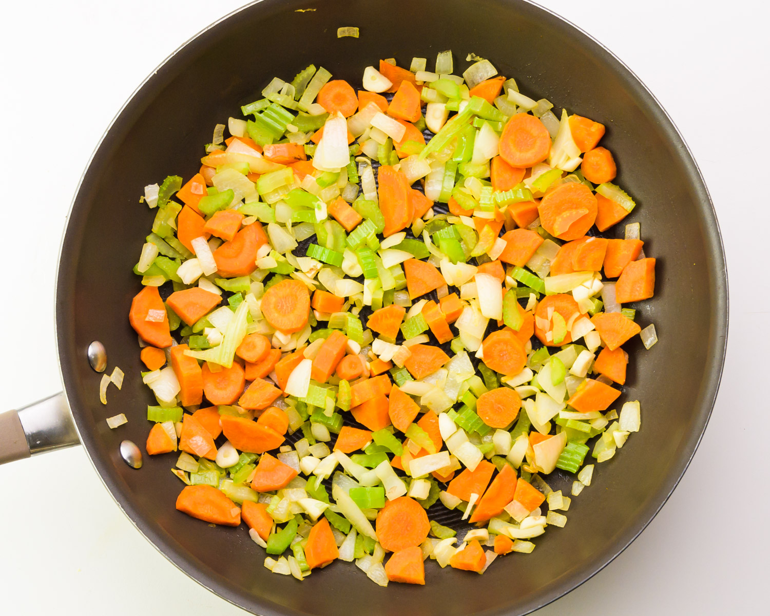 Carrots, onions, and celery are being cooked in a skillet.