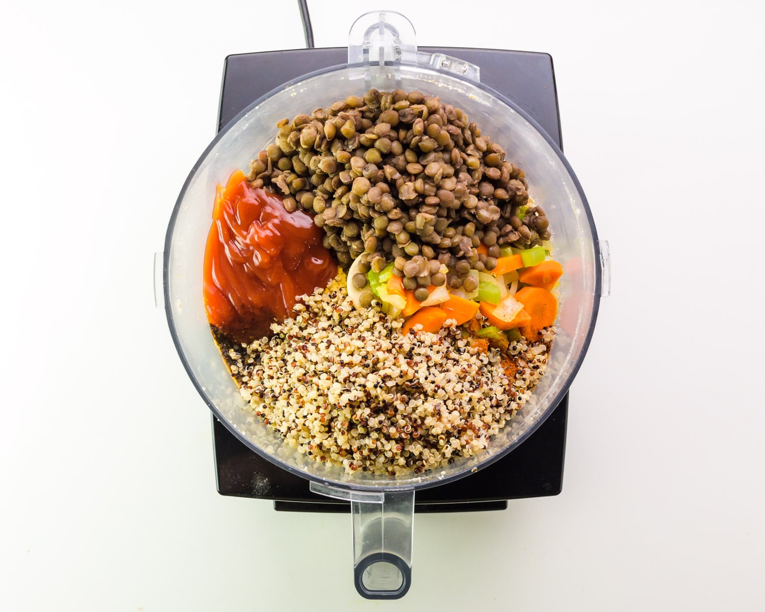 Lentils and other ingredients are in the bottom of a food processor bowl.