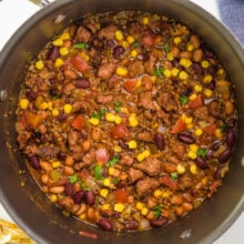 Looking into a pot full of vegan taco soup. There's a spoon on the right, seasonings and tortilla strips on the left.