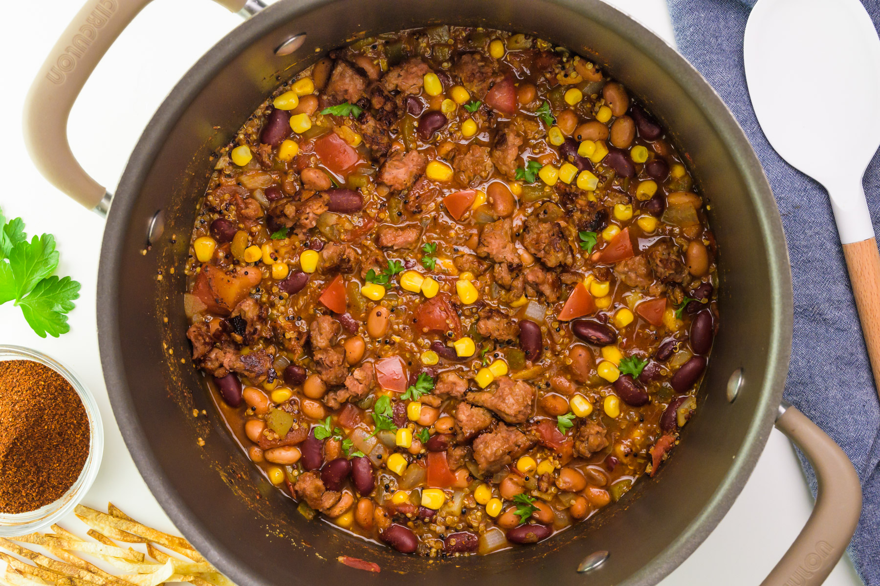 Looking into a pot full of vegan taco soup. There's a spoon on the right, seasonings and tortilla strips on the left.