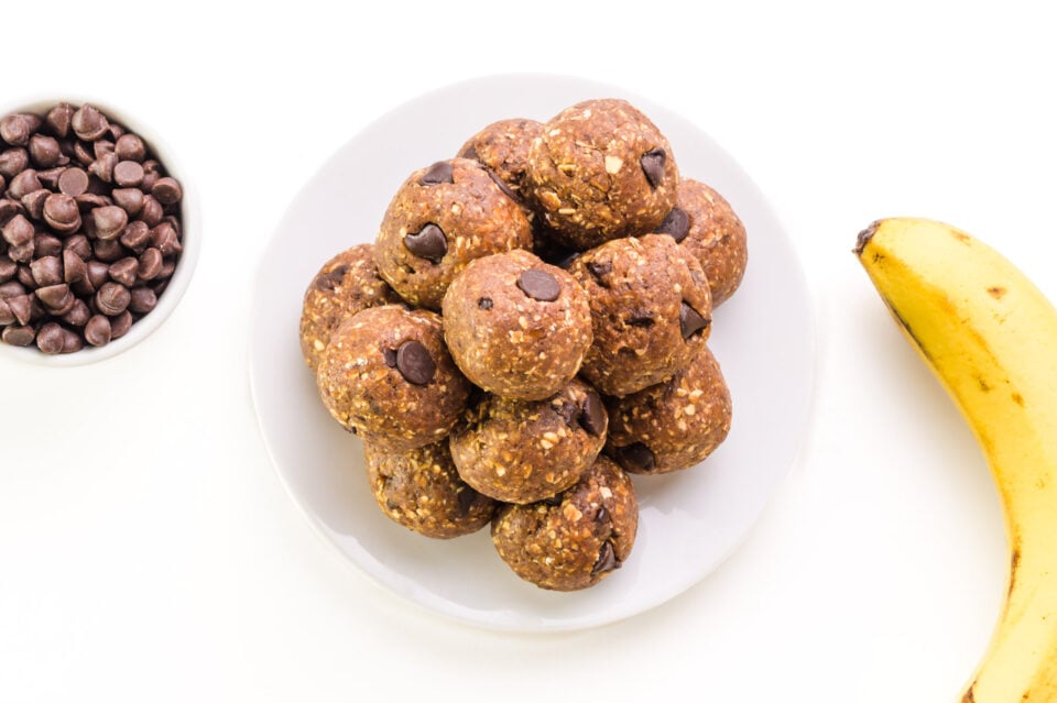 Looking down on a plate of energy balls sitting next to a bowl of chocolate chips and a banana.