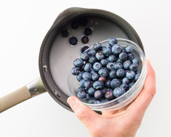 Blueberries are being added to a saucepan with a cornstarch mixture.