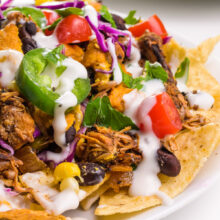 A plate of jackfruit nachos has chopped jalapeños, sour cream, and more as toppings. There's another plate in the background.