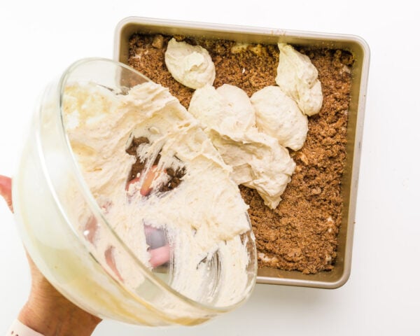 batter is being poured from a bowl over filling in a cake pan.