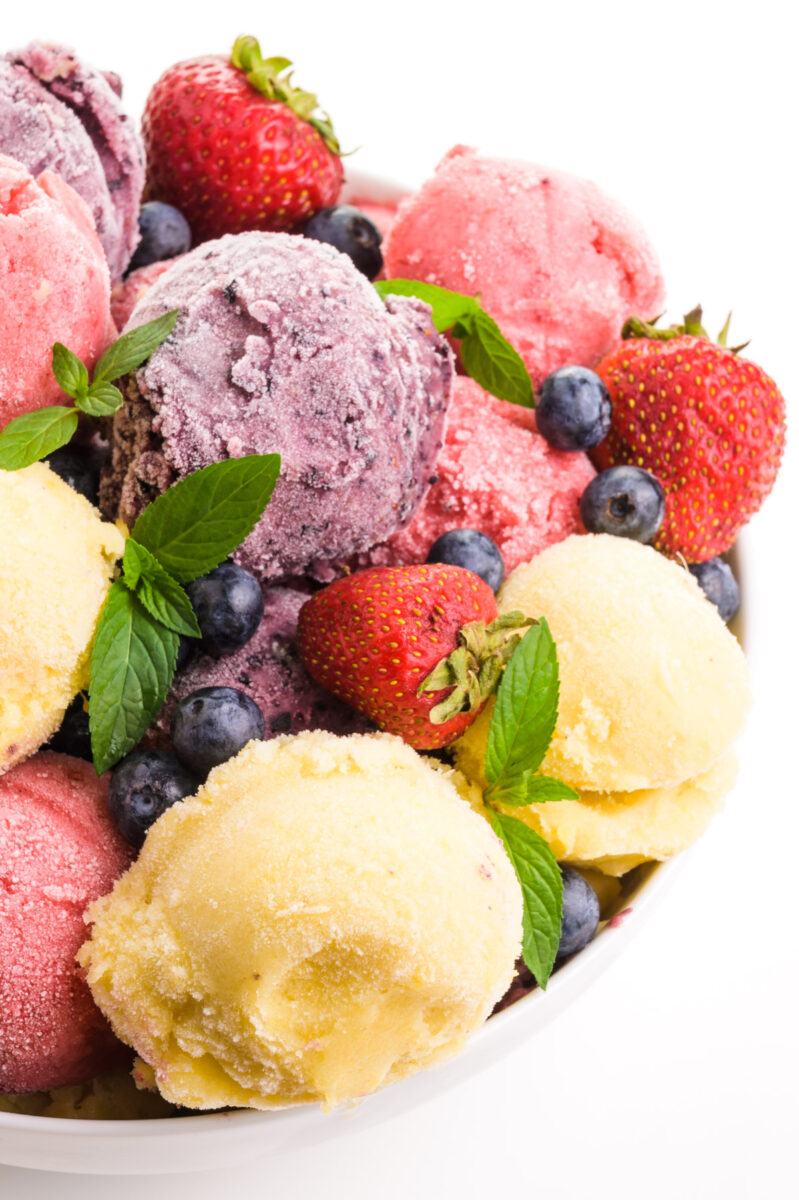 A large bowl holds dishes of different dairy-free frozen yogurt, such as berry, pineapple, and strawberry.