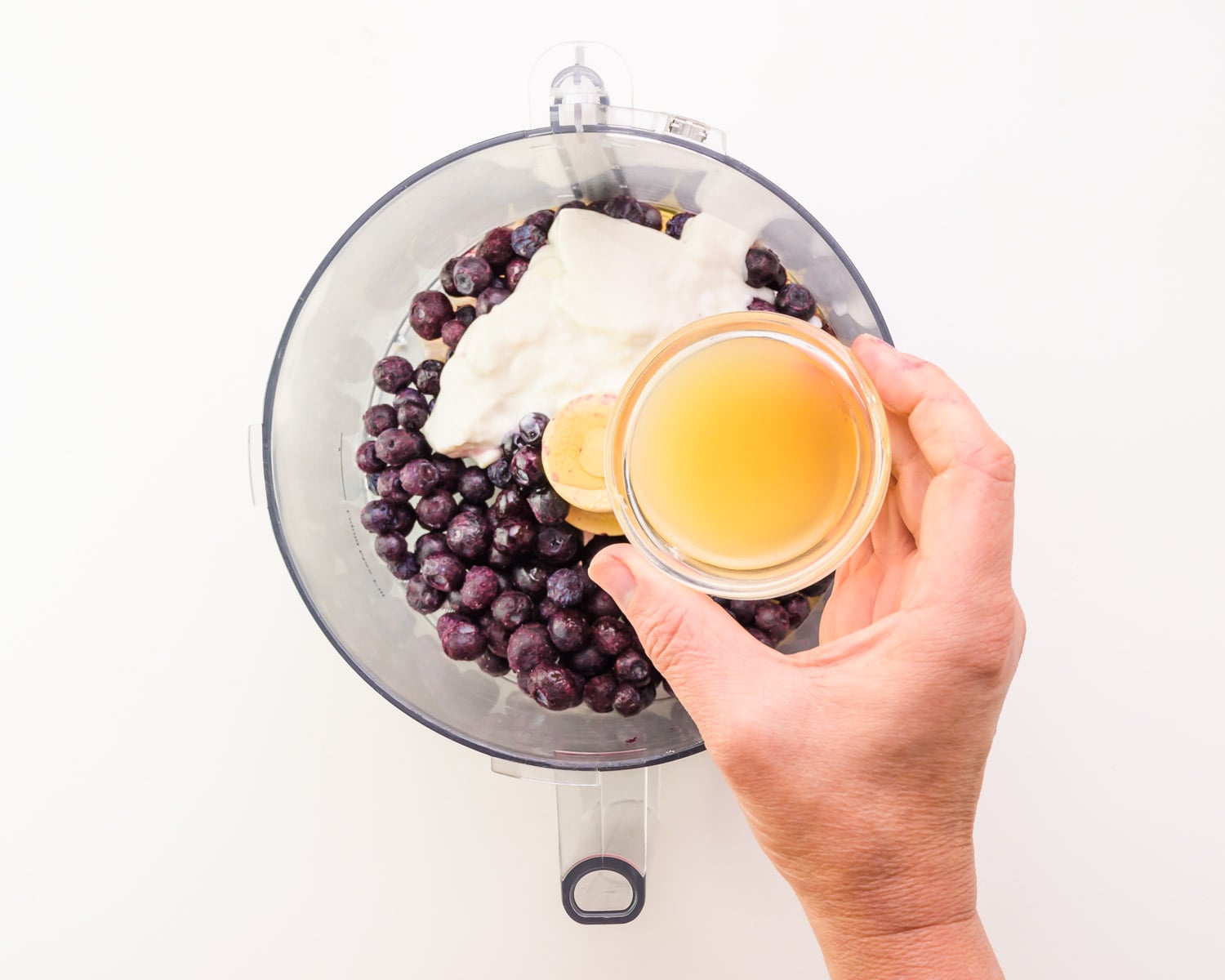 Lemon juice is being poured into a food processor bowl with berries and yogurt.