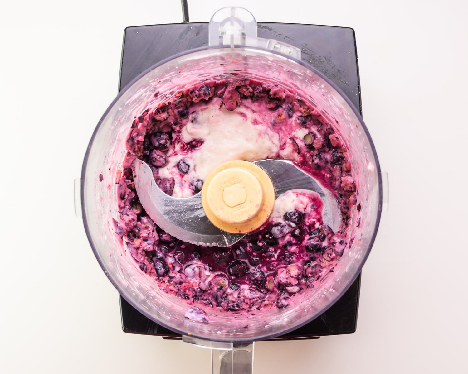 A blueberry yogurt mixture is in the bottom of a food processor.