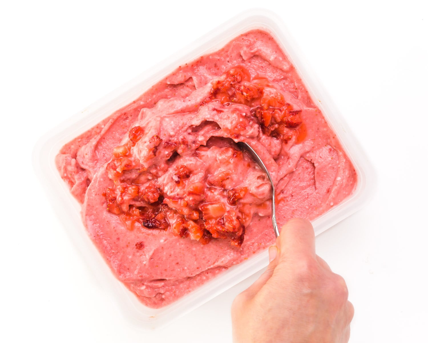 Mashed fresh fruit is being stirred into a container with frozen yogurt.