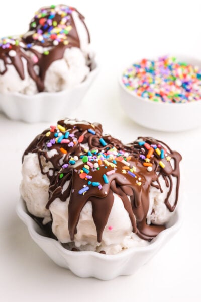 Two bowls of ice cream has chocolate magic shell topping and sprinkles. A bowl of sprinkles sits on the background.