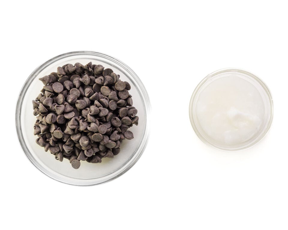 A bowl of chocolate chips and coconut oil sit on a white counter.