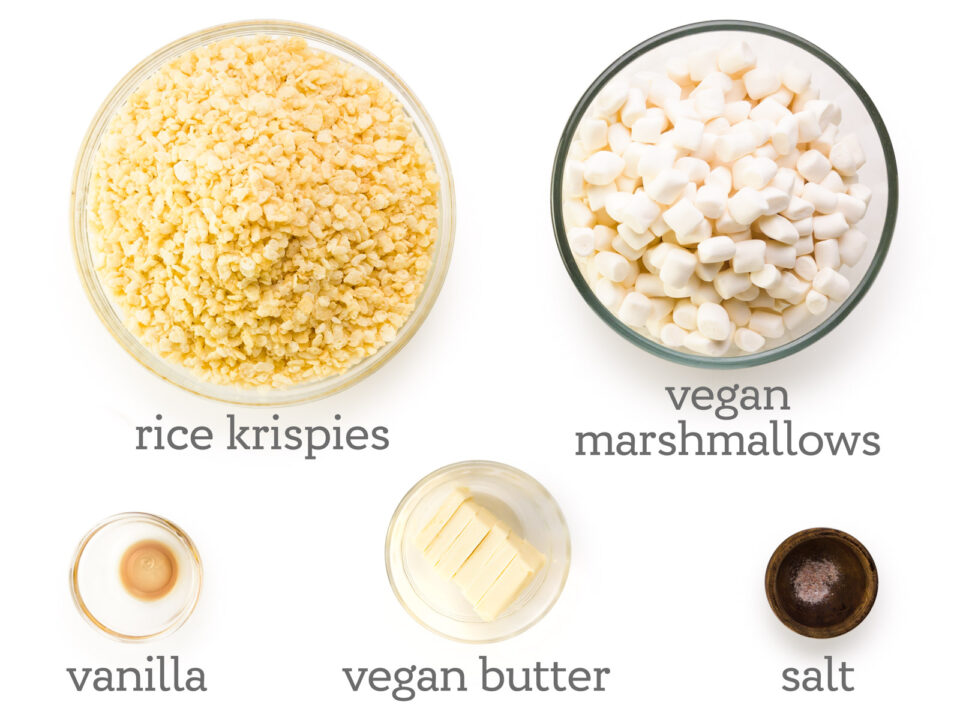 Ingredients are laid out on a white table, including Rice Krispies, vegan marshmallows, salt, vegan butter, and vanilla.