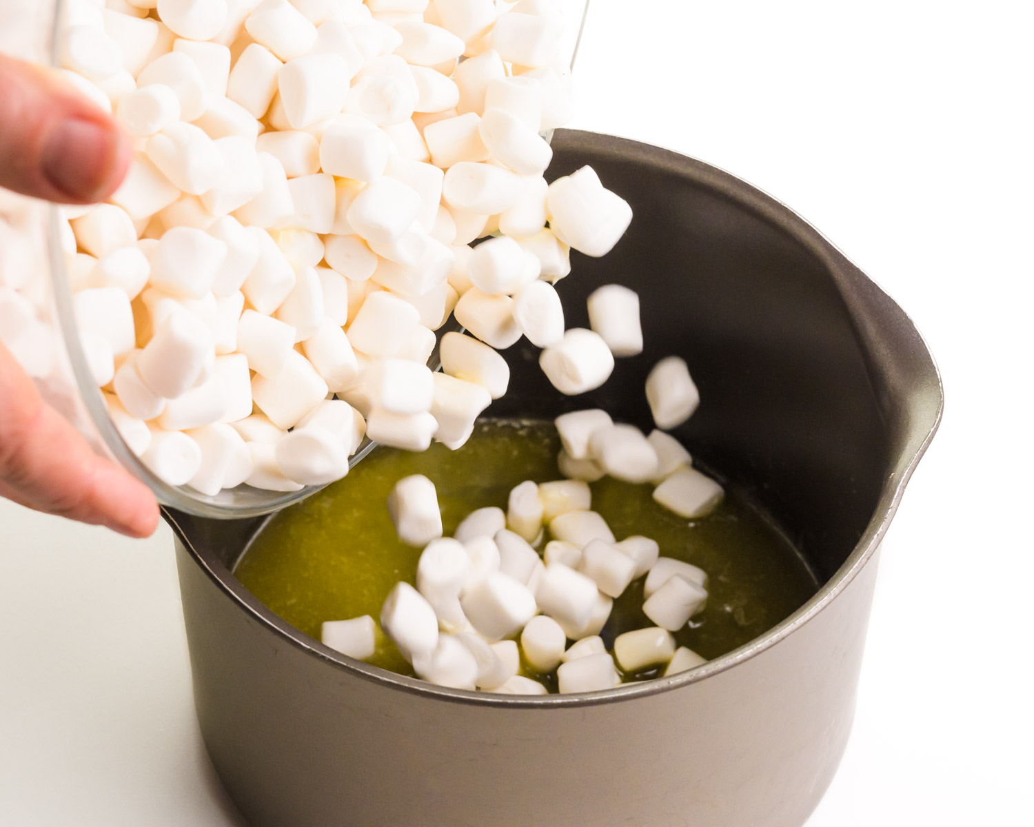 Marshmallows are being poured from a bowl into a saucepan with melted butter.
