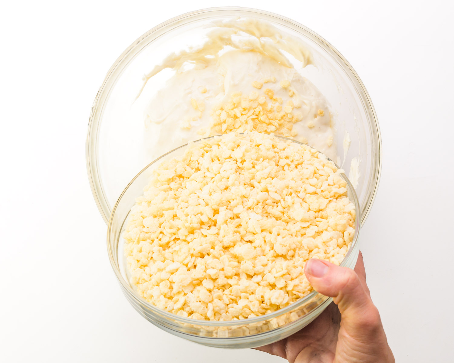 A hand pours cereal from bowl into a larger bowl with melted marshmallows.