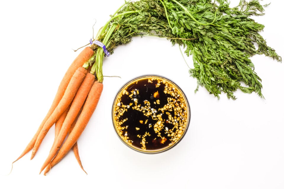 Fresh carrots sit next to a bowl of marinade.