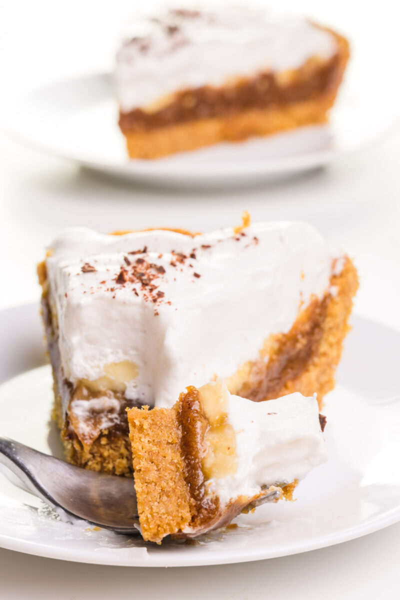 A bite of pie sits on a fork, sitting in front of the rest of the pie. There is another pie on a plate in the background.