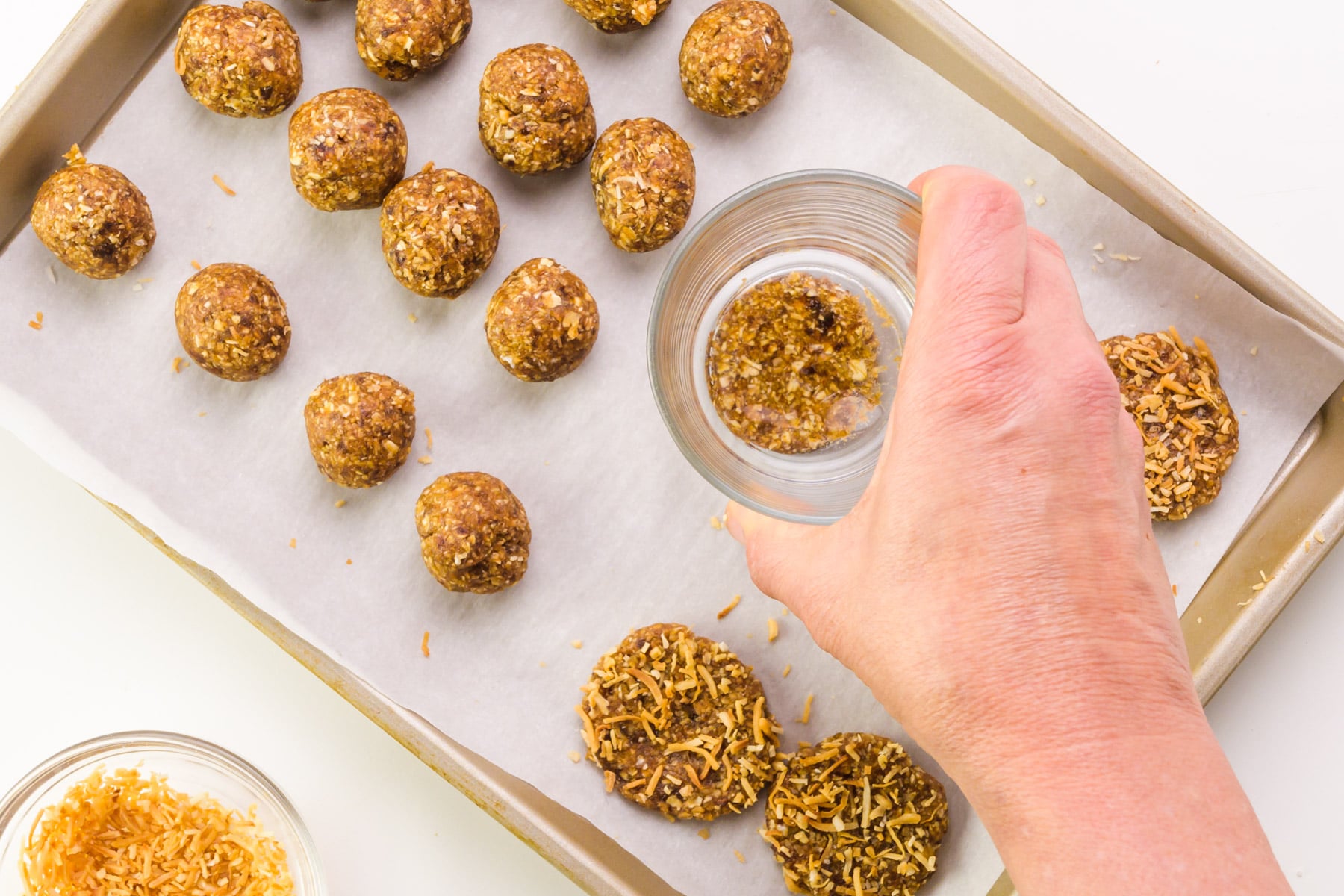 A hand holds a glass, pressing cookie dough balls into flat discs.