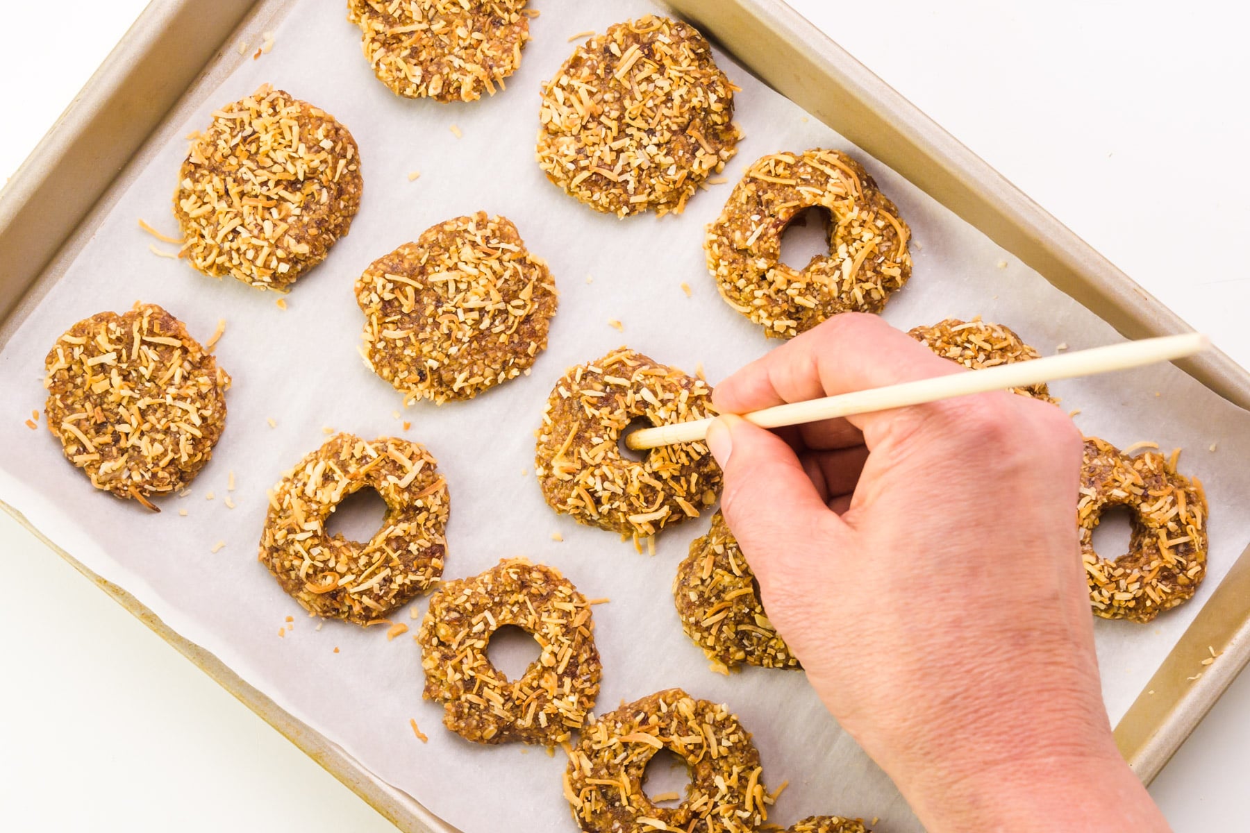 A hand holds a skewer, creating wholes in flattened cookie dough discs.