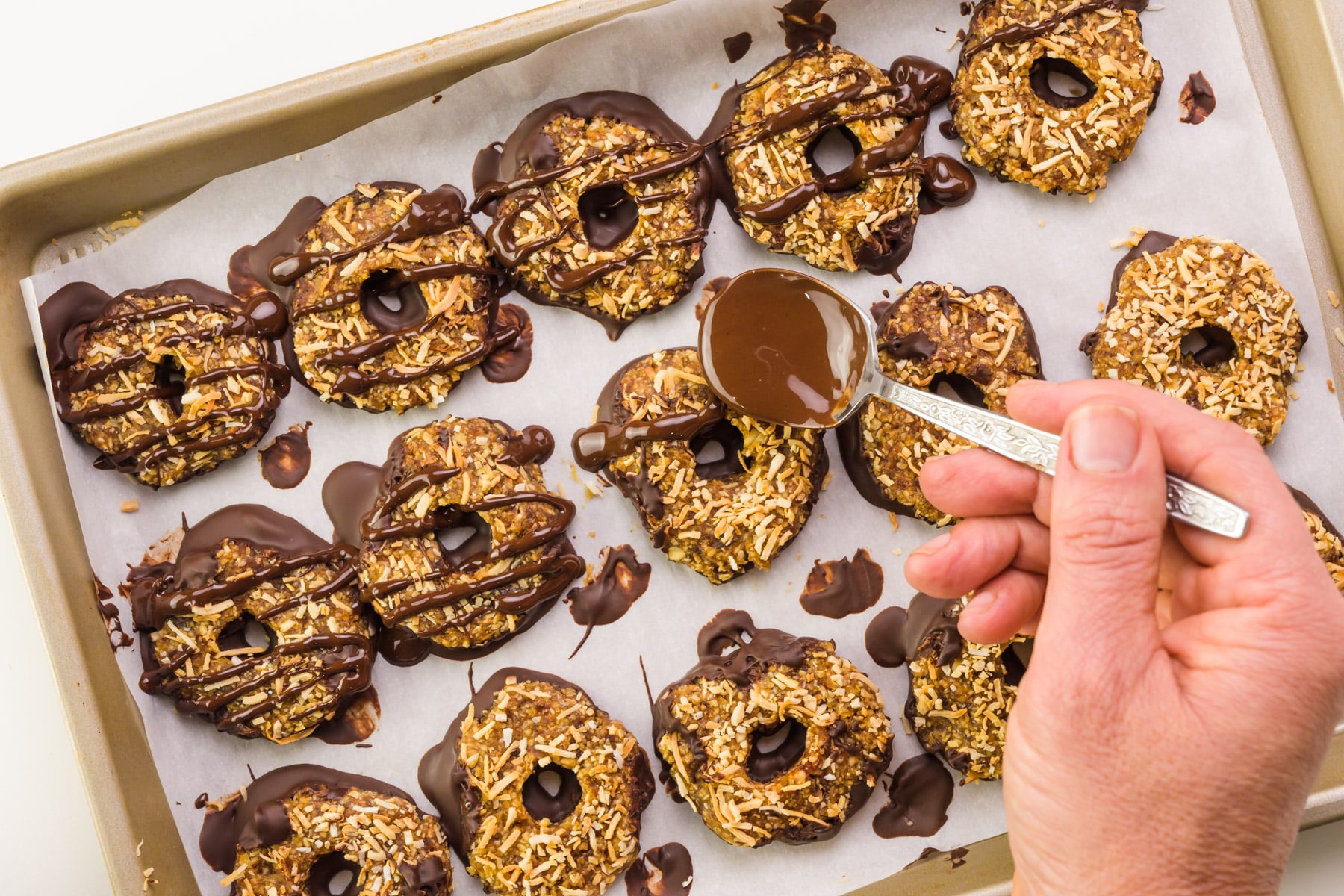 A hand drizzles chocolate over the top of rows of cookies.