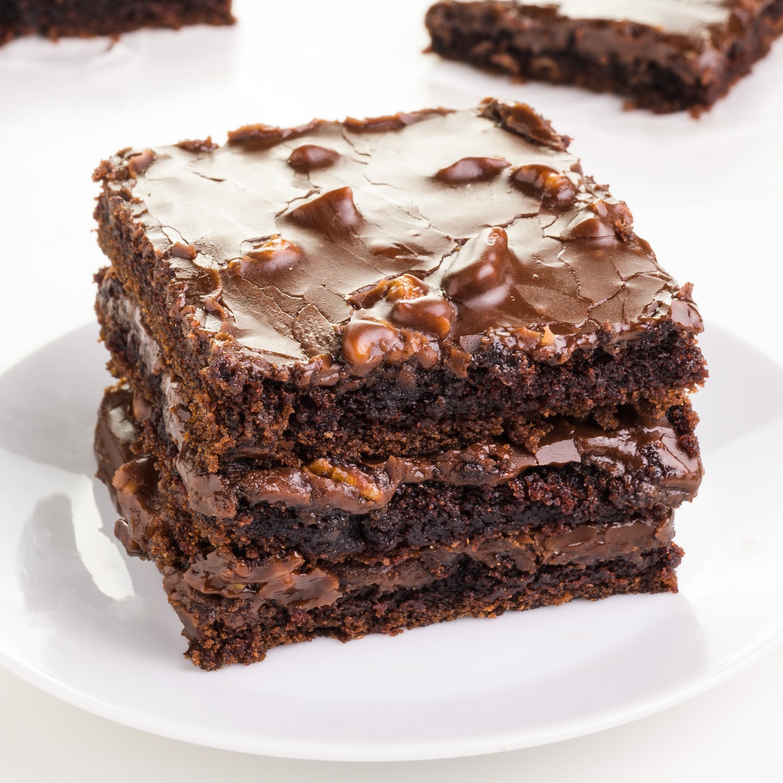 A stack of vegan Texas sheet cake slices sits on a plate. There are more slices in the background.