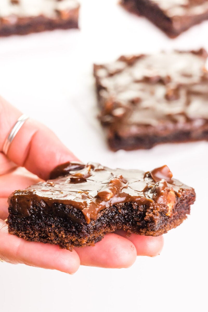 A hand holds a slice of vegan sheet cake with a bite taken out. There are more slices in the background.