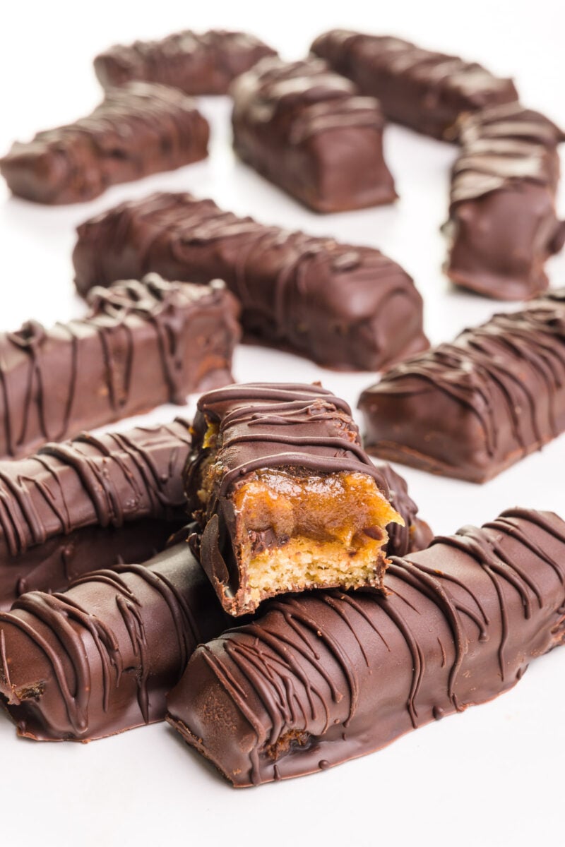 A healthy Twix bar has a bite taken out and sits on other Twix bars. There are more in the background.
