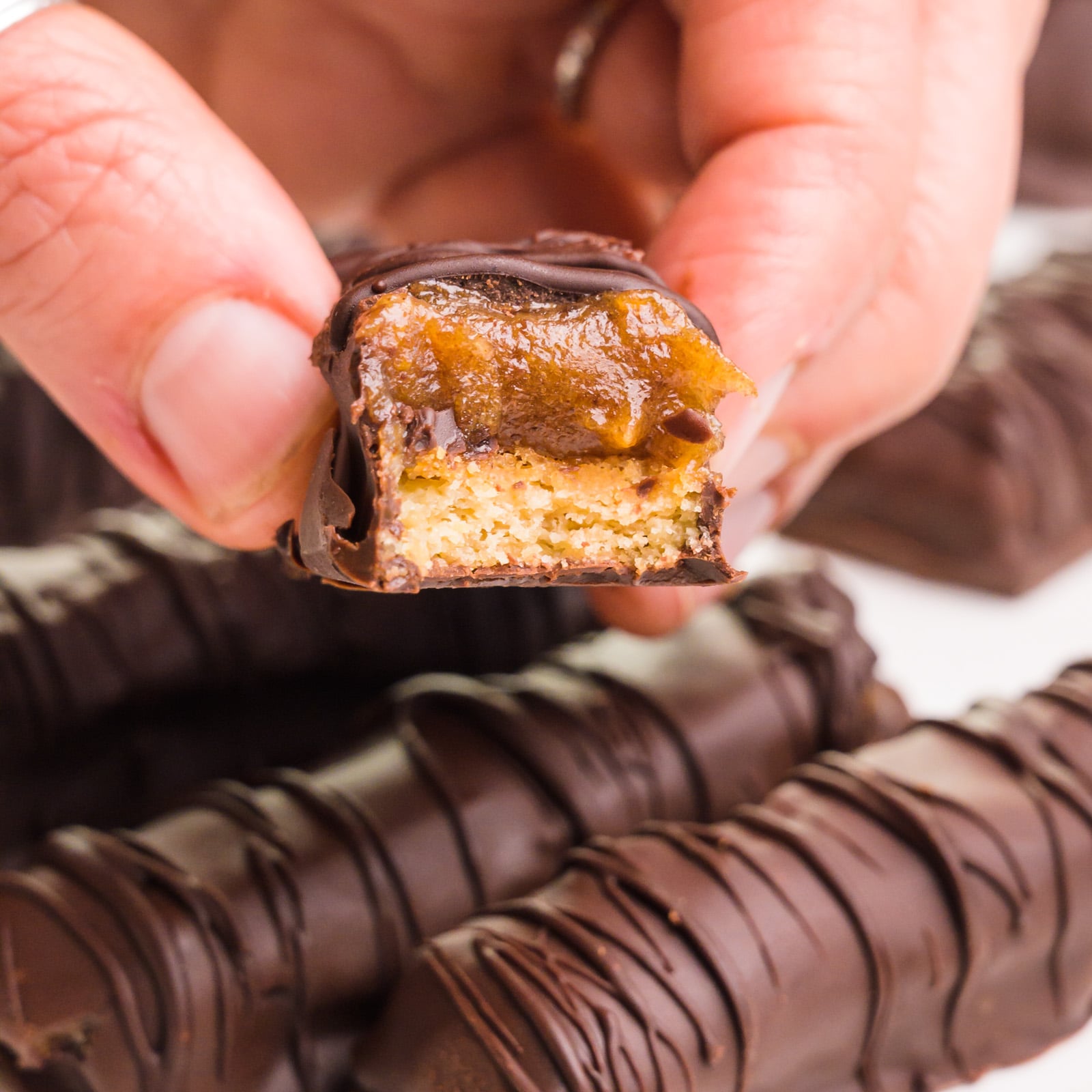 A hand holds a vegan twix bar with a bite taken out. It hovers over more bars.