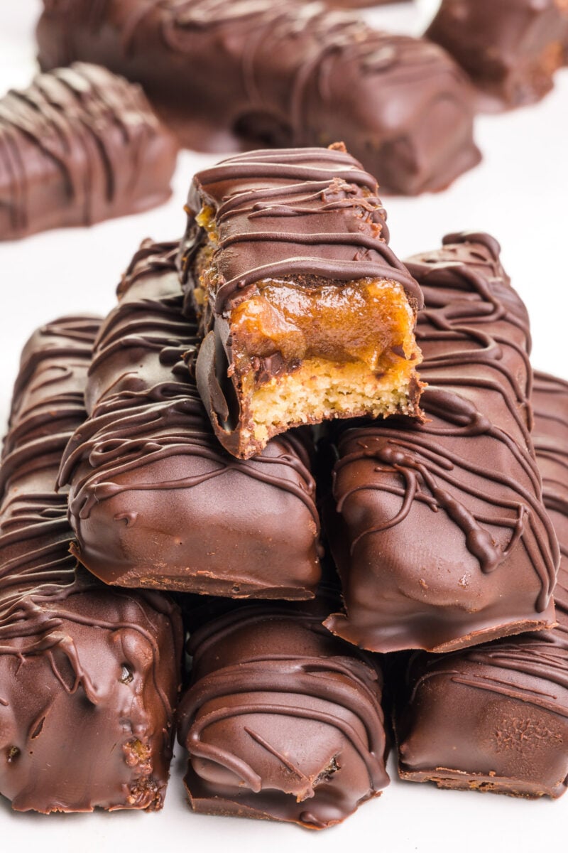 A vegan Twix with a bite taken out sits on top of more Twix bars.