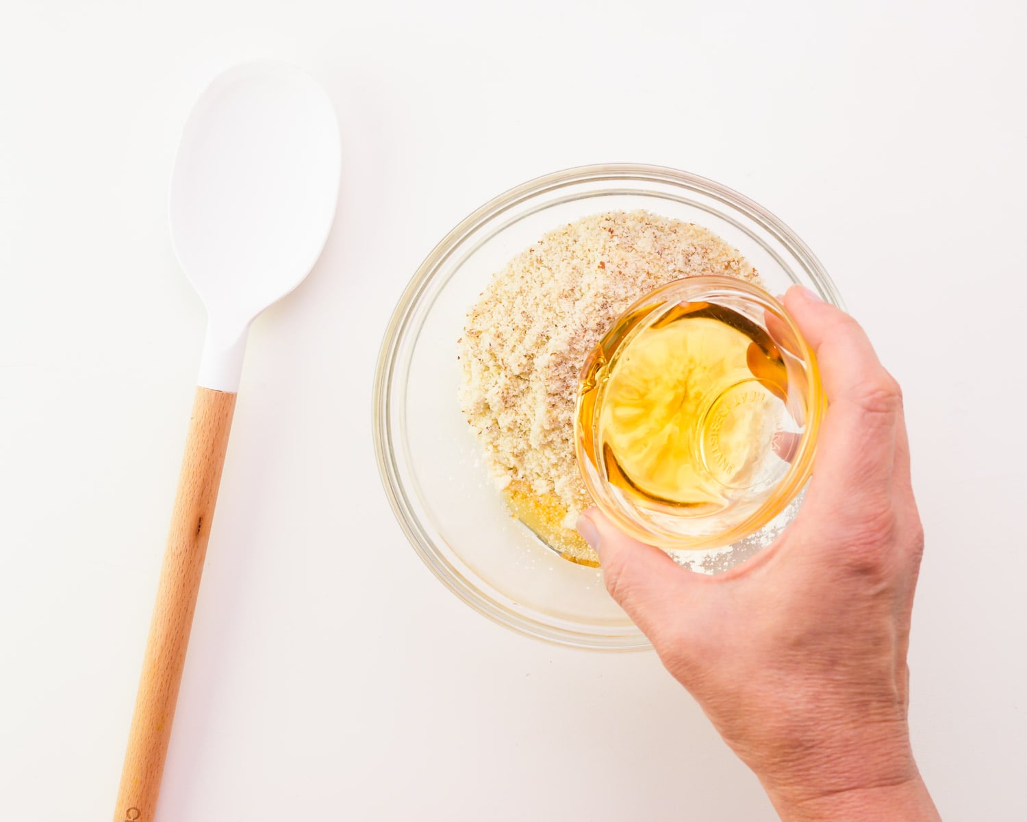 Maple syrup is being poured into a bowl with flour. There is a white spatula next to the bowl.