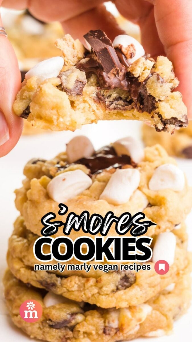 A hand holds a cookie with a bite taken out, hovering over a stack of more cookies. The text reads, S'mores Cookes, Namely Marly Vegan Recipes.