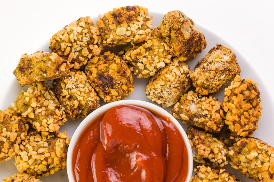Looking down on a plate of cauliflower tater tots sitting next to a bowl of ketchup.