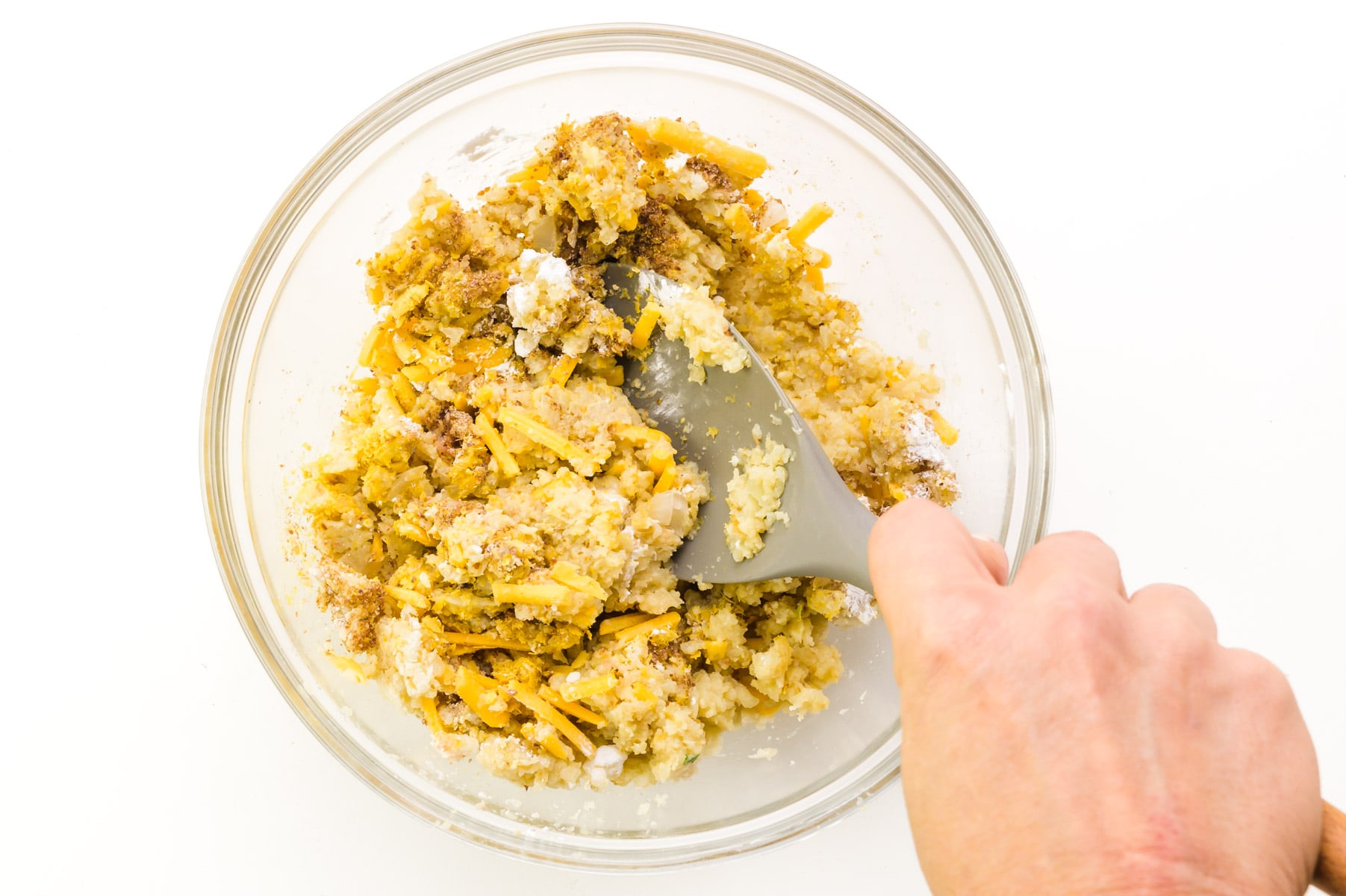 A hand holds a spatula, stirring together ingredients in a bowl.