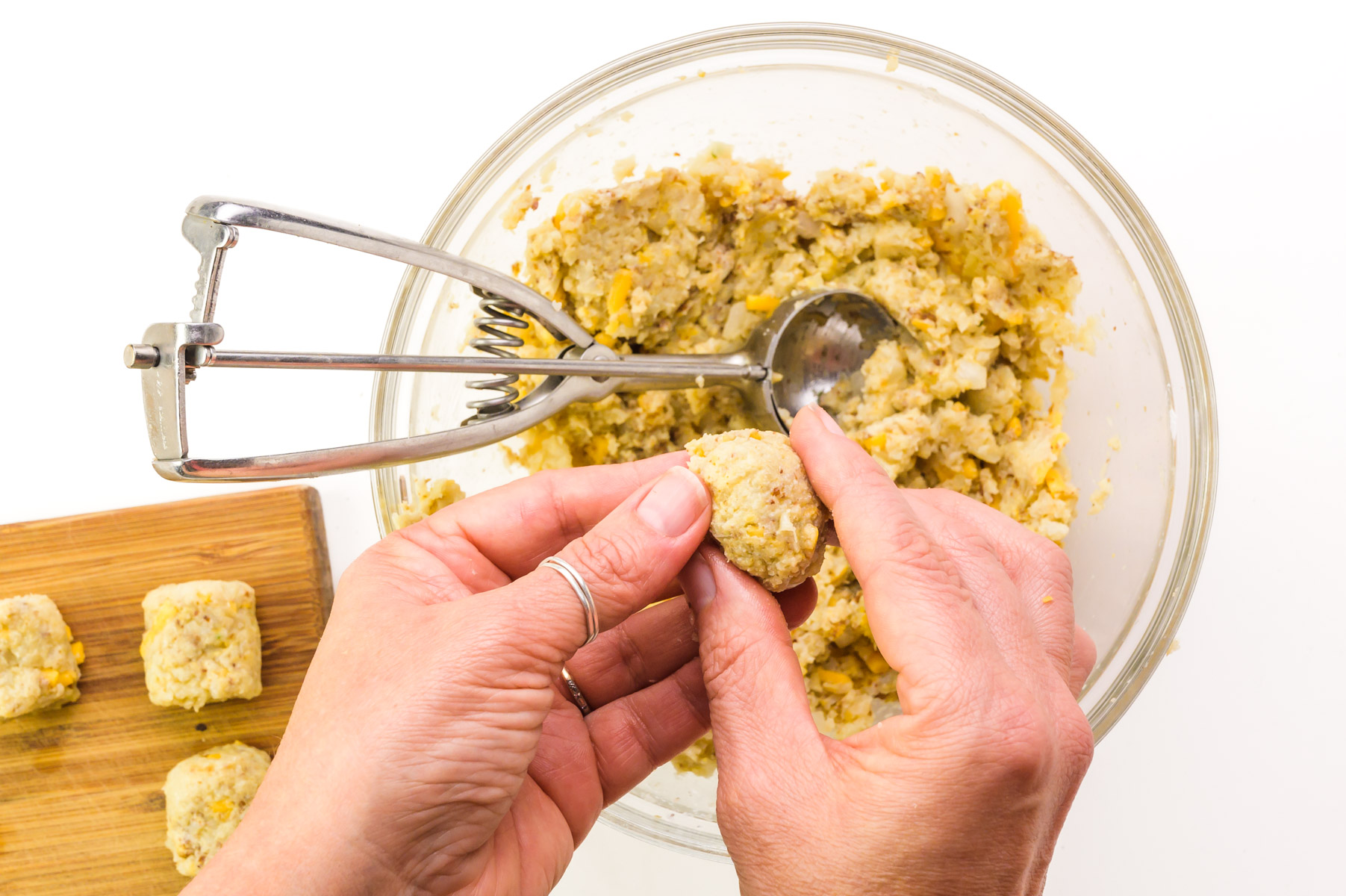 Two hands are forming dough into tot form. There is a wooden cutting board with tots on it.