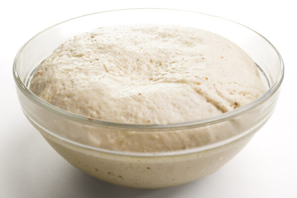 Dough is rising in a glass bowl.