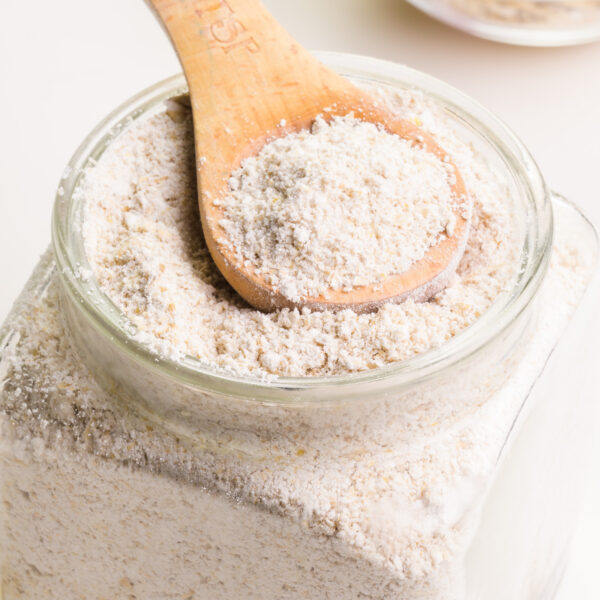 Looking into a bowl of oat flour with a wooden measuring spoon in it.