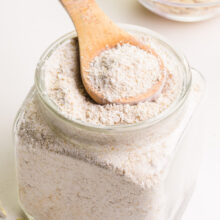 A wooden spoon sits in a bowl of oat flour. There is a bowl of oats in the background.