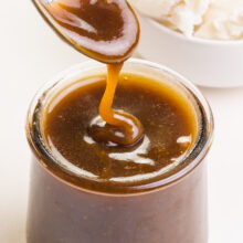 A spoon drizzles dairy-free butterscotch sauce over a jar with more sauce in it.