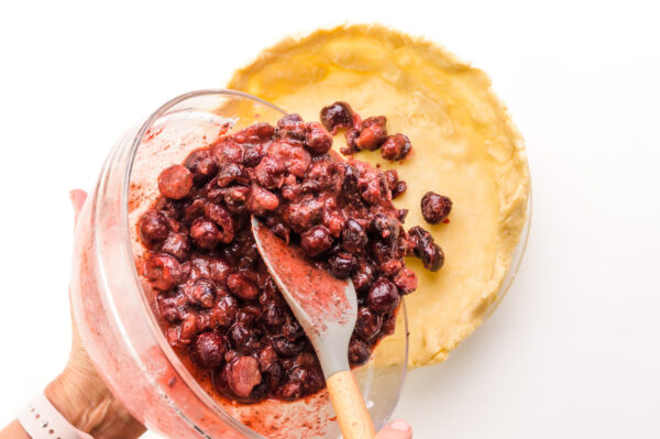 Cherry pie filling is being spooned into an unbaked crust.