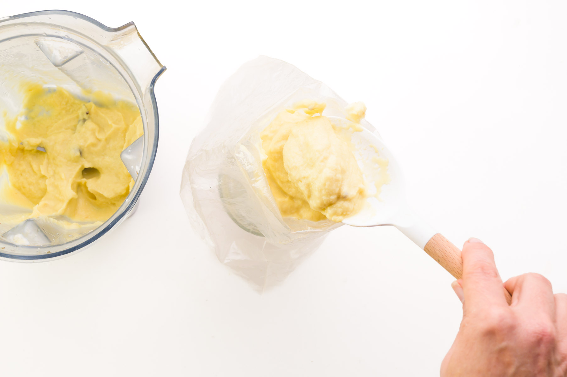 A hand holds a spatula, transferring dole whip from a blender to a piping bag.