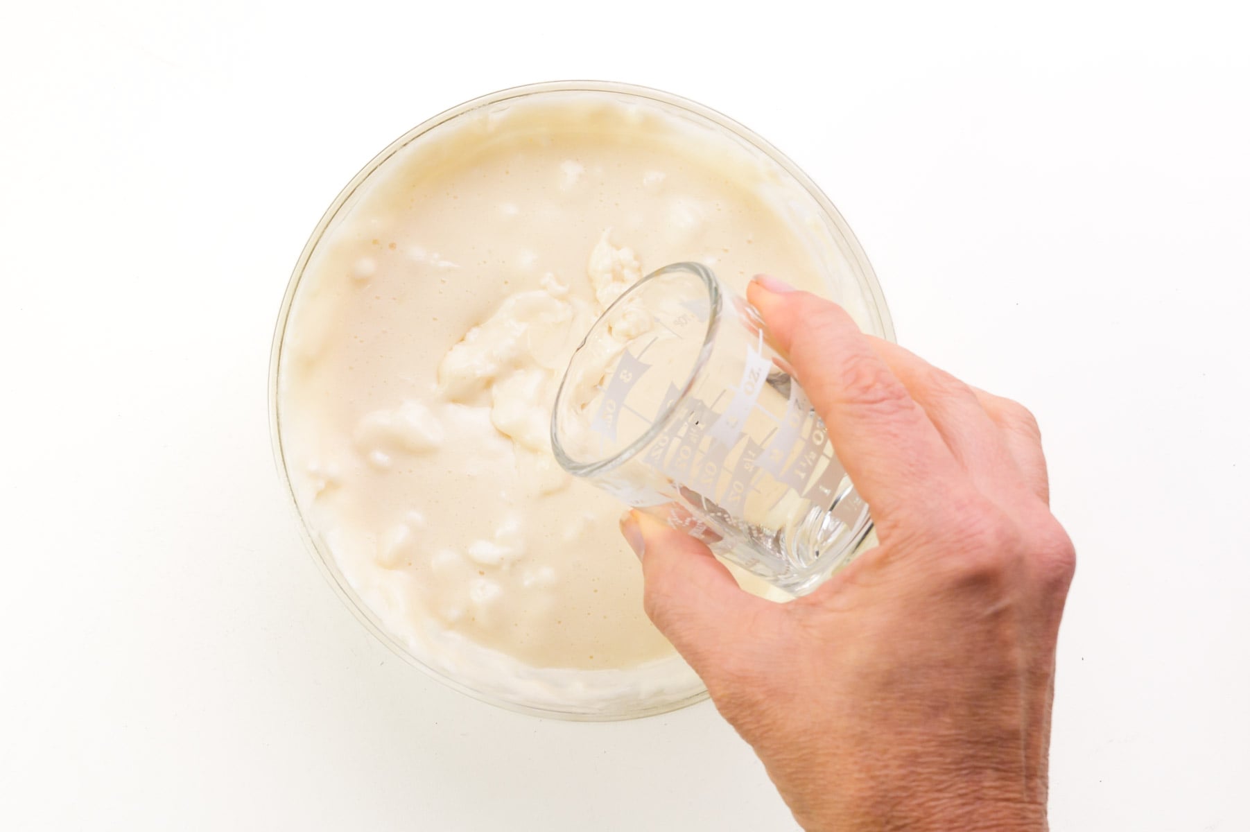 A hand pours creme de menthe into a bowl of melted marshmallows.