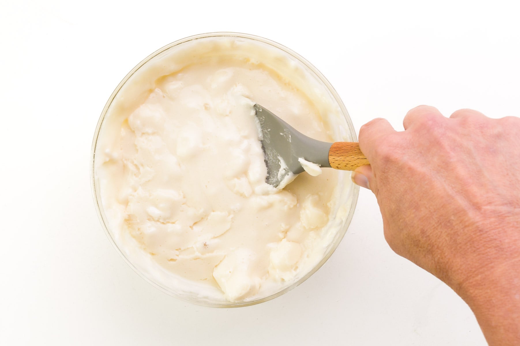 hand holds a spatula, stirring together a melted marshmallow mixture.