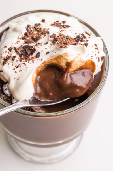 Looking down into a spoon in a bowl of vegan pudding with whipped cream on top.