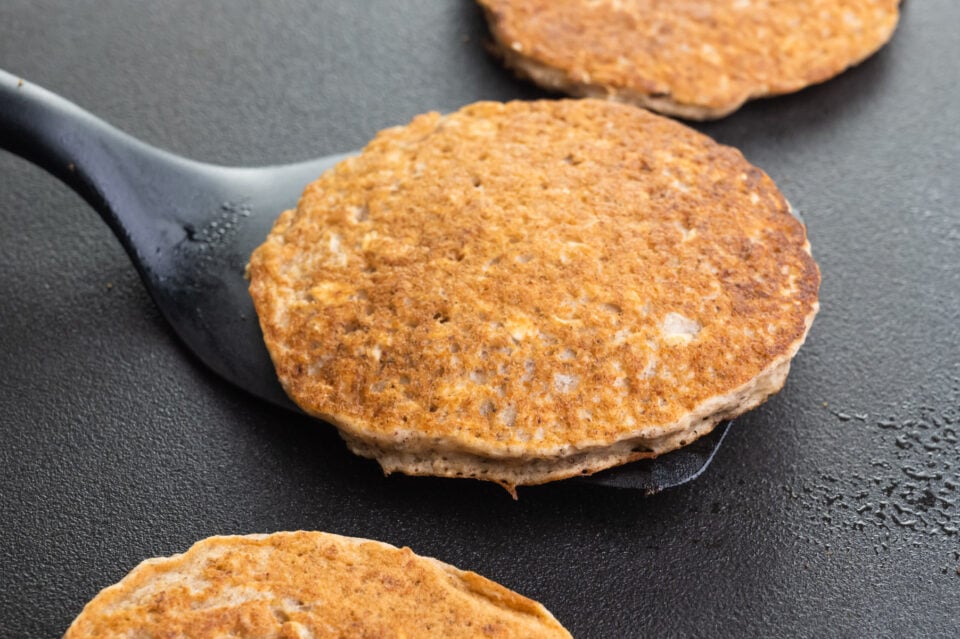 A spatula holds a pancake on a griddle, getting ready to flip it. There are other pancakes on the griddle, too.