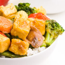Crispy tofu stir fry features colorful veggies on top of rice in a bowl.