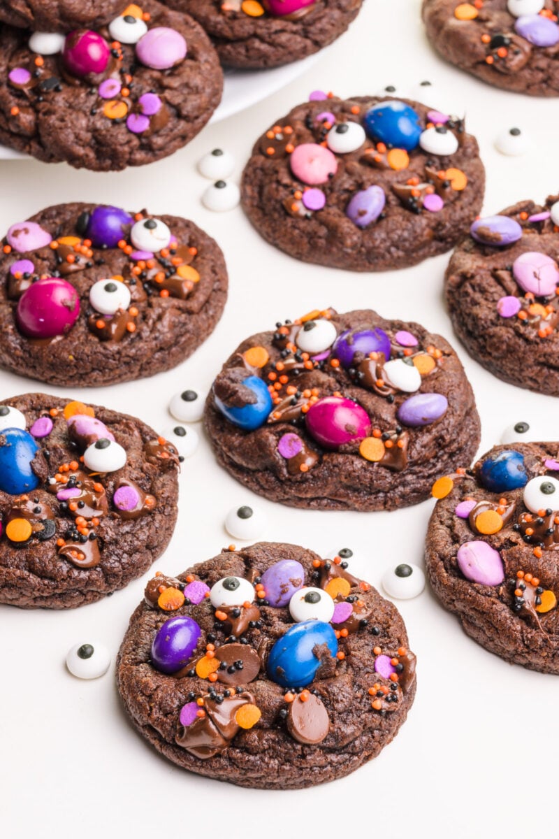 Colorful chocolate Halloween cookies sit next to each other on a white table. There are candy eyes between the cookies.
