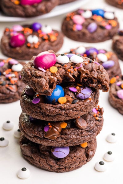 A stack of vegan Halloween cookies shows the top one with a bite taken out. There are more cookies in the background.