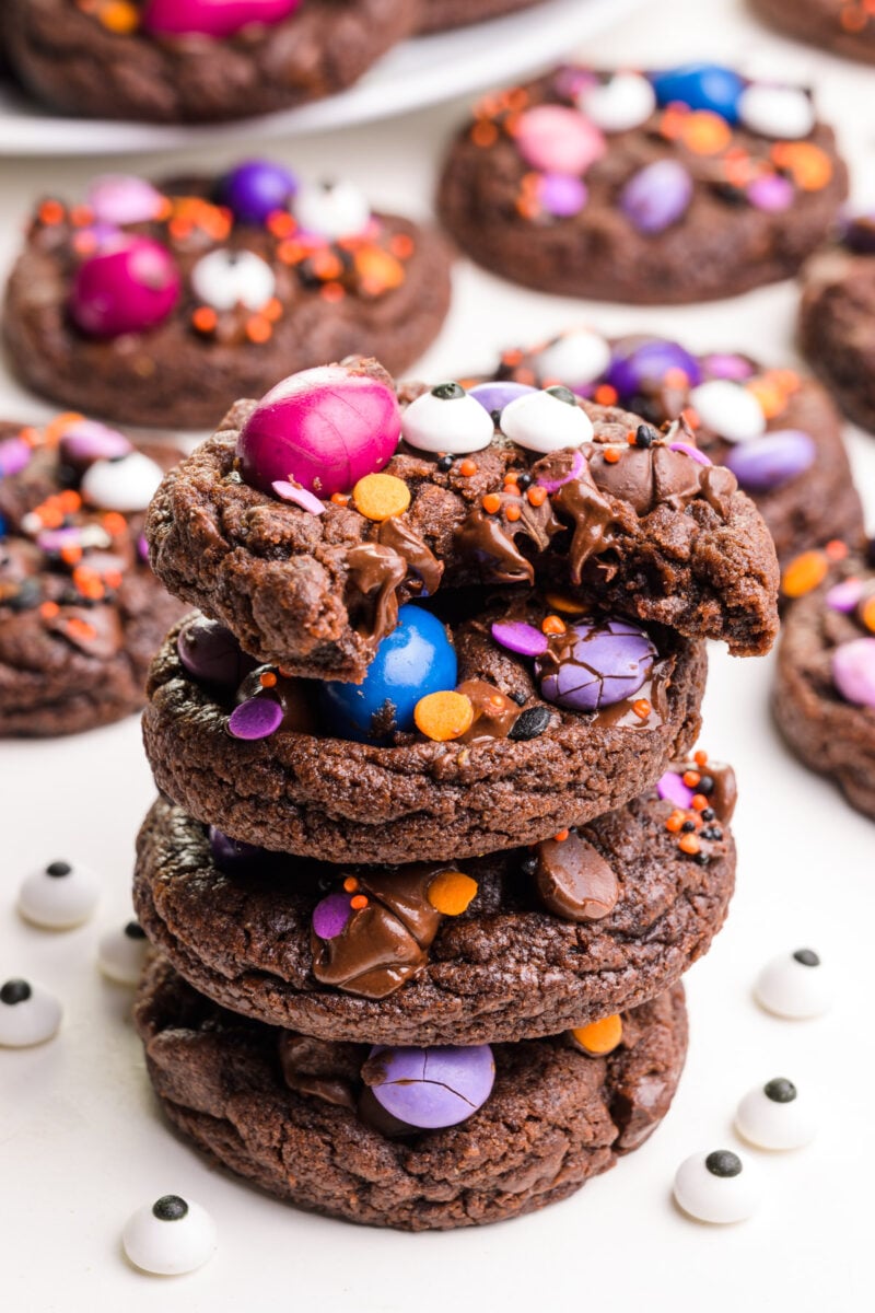 A stack of vegan Halloween cookies shows the top one with a bite taken out. There are more cookies in the background.